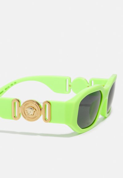 Occhiali da sole verdi in plastica con una montatura rettangolare spessa, lenti scure e un accento dorato con un emblema di leone sulle tempie.