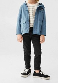 Vaaleansininen huppari, jossa on kaksi etupainiketta, raidallinen paita alla, mustat farkut ja mustat tennarit, joissa on valkoiset nauhat.