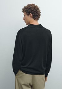 Svart långärmad polo skjorta i mjukt material, med klassisk krage och avslappnad passform, med synliga sömmar vid axlarna.