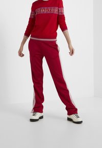 Suéter rojo con canesú estampado y letras blancas, combinado con pantalones deportivos rojos con franjas laterales blancas. Modelo con zapatos blancos.