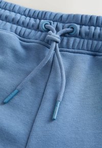 Pantalon de jogging bleu clair en gros plan montrant une ceinture élastique avec un cordon noué et la texture du tissu.