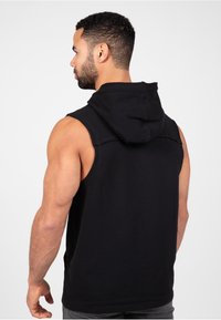 Zwarte mouwloze hoodie met een trekkoord. Gemaakt van zachte stof, heeft een ontspannen pasvorm en stiksel details op de schouders.