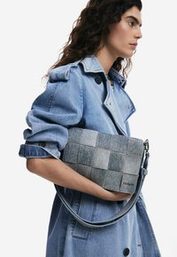 Borsa a tracolla in denim con un design a patchwork in diverse sfumature di grigio. Presenta una tracolla removibile e dettagli di cucitura sottili.