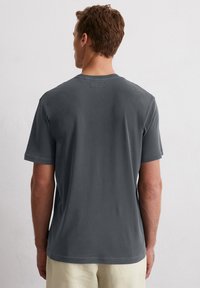 Donkergrijze korte mouwen T-shirt met een ronde hals, zachte textuur, eenvoudig ontwerp en een minimalistisch achterlabel. Gecombineerd met lichte broeken.