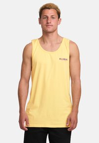 Camiseta de algodón sin mangas de color amarillo con un pequeño logo rojo en el pecho. El diseño es sencillo, con un escote redondo y un corte relajado.