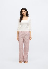 Bijela majica dugih rukava sa kvadratnim izrezom i malim logom, uparena s širokim ružičasto-bijelim prugastim hlačama za spavanje. Mekana tkanina, opušteni kroj.