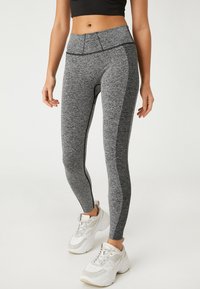 Leggings gris en tissu texturé, taille haute, avec des panneaux latéraux contrastants. Portés avec des baskets blanches épaisses.
