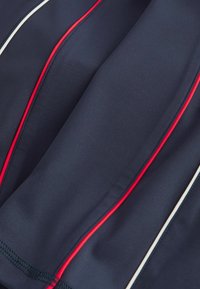 Tamno plava tkanina s crvenim i bijelim vertikalnim prugama, glatke teksture i šivenim rubovima. Materijal izgleda rastezljivo i lagano.