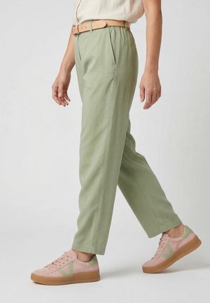 Person iført lysegrønne bukser med højtalje og sidelommer, et beige bælte og pink sneakers med grønne accenter og gummisåler.