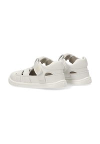 Sandalias blancas de cuero suave, con puntera cerrada, correa de velcro y diseños troquelados para ventilación. Plantilla suave y texturizada.