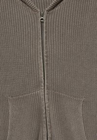 Hoodie zippé en maille de couleur taupe avec une surface texturée, doté de deux poches avant et d'une fermeture éclair métallique.