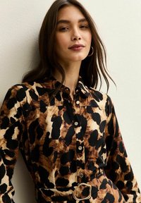 Leopardprinthemd in bruin, zwart en roomkleur; met een kraag, knoopsluiting en een riem met een gouden gesp.