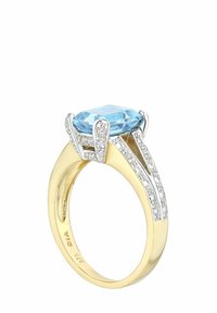 Zlatni prsten s velikim ovalnim plavim dragim kamenom, postavljenim u srebrne uške, s dijamantnim naglascima duž trake za dodatni sjaj i detalje.