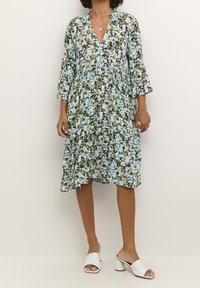 Robe fleurie en bleu, vert et blanc avec un décolleté en V et des manches trois-quarts. Forme évasée avec une silhouette fluide et une taille froncée.