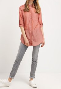 Laxfärgad skjorta med knappar och uppkavlade ärmar, med en bröstficka, tillsammans med ljusgråjeans och vita sneakers.