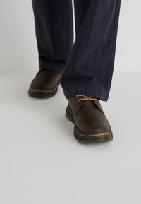 Rjave usnjene čevlje z zaobljenim nosom, rumenimi vezalkami in rumenimi poudarki. Uporabljeni z temno prugastimi hlačami.