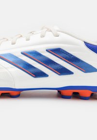 Scarpa da calcio bianca con dettagli blu e arancioni. Presenta tre strisce blu, superficie testurizzata e suola arancione con tacchetti per la trazione.