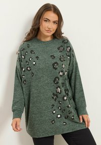 Pull vert à manches longues, avec un motif léopard en noir et accents argentés. Fabriqué dans un tissu doux et texturé.