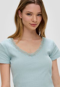Jasnoniebieska bluzka z krótkim rękawem o prążkowanej teksturze, z dekoltem w kształcie litery V ozdobionym delikatną koronką.