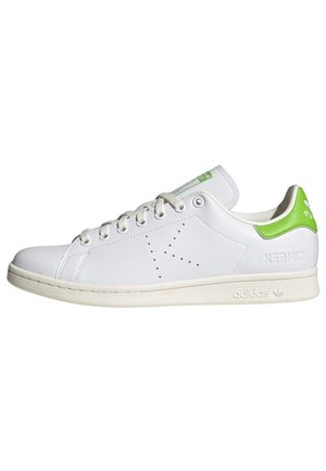 Baskets basses blanches Adidas avec languette de talon verte, "K" perforé sur le côté, et "Kermit" embossé près de la semelle.