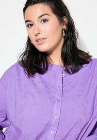 Camicia viola con bottoni, decorata con motivi floreali testurizzati, dotata di colletto e bottoni sulla parte anteriore. Tessuto morbido con una vestibilità rilassata.