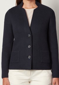 Marinblå texturerad cardigan med rund halsringning, fem-knappsstängning och två framfickor. Materialet är mjukt och designen är figursydd.