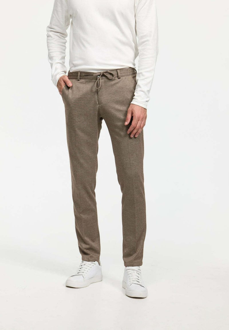 Pantalons bruns ajustés en tissu texturé avec une taille élastique à cordon de serrage et des poches latérales, associés à des baskets blanches.