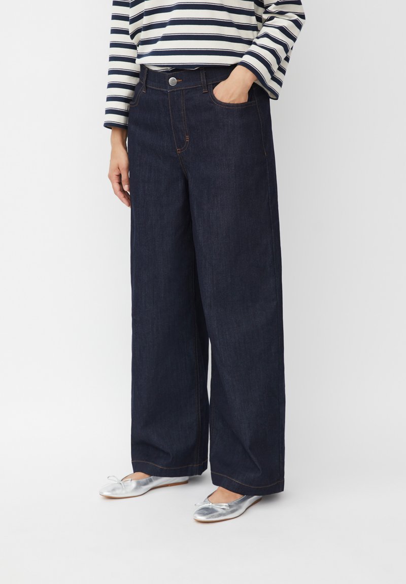 Jeans anchos de color azul oscuro con una cintura alta, cinco bolsillos y costuras en contraste sutil, combinados con bailarinas plateadas.