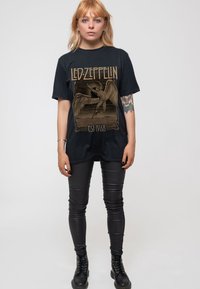 Black oversized t-shirt featuring a gold Led Zeppelin graphic with a figure and wings; paired with black skinny jeans and combat boots.