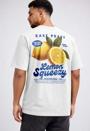 Man wearing white tee showing back print with lemons and text "Easy Peasy Lemon Squeezy" in blue and yellow colors.