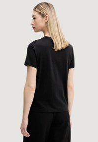 T-shirt nera a maniche corte con collo rotondo, texture liscia e vestibilità ampia, progettata con cuciture minime e senza grafiche.