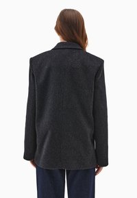 Tummanharmaa villa-blazer, jossa on muotoutunut siluetti, viistot läpät ja pitkät hihat. Sisältää puhtaita linjoja ja minimaalista ompelutusta.