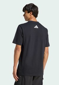 T-shirt en coton noir avec manches courtes, coupe décontractée et logo Adidas blanc dans le haut du dos. Associé à un pantalon cargo foncé.