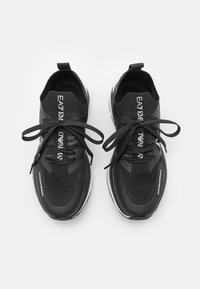 Svarta sportskor med ovandel i mesh-material, rund tå, platta snören och en framträdande logotyp. Tjock sula med vita accenter. Inga synliga mönster.