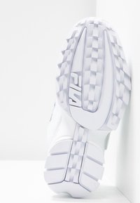 Sneaker bianco con suola in gomma testurizzata, caratterizzata da un motivo geometrico e un logo ben visibile. La tomaia è realizzata in materiale sintetico liscio.
