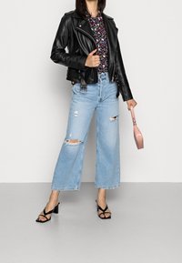 Svart läderbikerjacka, blommig blus, ljusblå vida jeans med hål, svarta klacksandaler och en rosa axelväska.