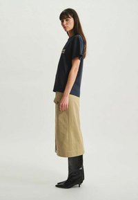 T-shirt marine à manches courtes avec texte imprimé. Jupe beige longueur cheville avec boutonnière sur le côté, associée à des bottines noires à talons et bouts pointus.