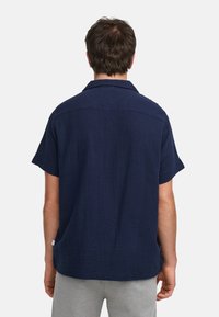 Camisa de manga corta azul marino hecha de tela texturada, con un corte holgado y cuello con solapa, con dobladillo recto y detalle de abertura lateral.
