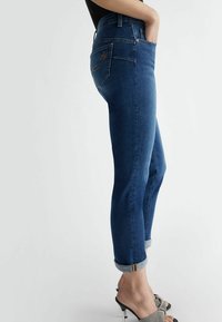 Jeans de mezclilla azul oscuro con corte ajustado, dobladillos enrollados y un bolsillo trasero con detalles bordados. Textura suave, diseño de talle medio.