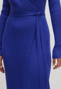 Blaues geripptes Strickkleid mit Wickeldesign, langen Ärmeln und einem gebundenen Gürtel. Verfügt über eine weiche Textur und einen leichten Glanz.