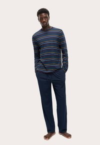 Long-sleeve striped shirt in navy, featuring horizontal multicolored stripes, paired with dark blue trousers. Fabric appears soft and relaxed.