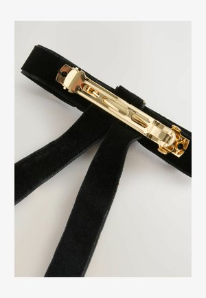 Čierne zamatové traky so zlatou kovovou sponou. Majú hladký povrch, široké popruhy a dekoratívne kovanie.