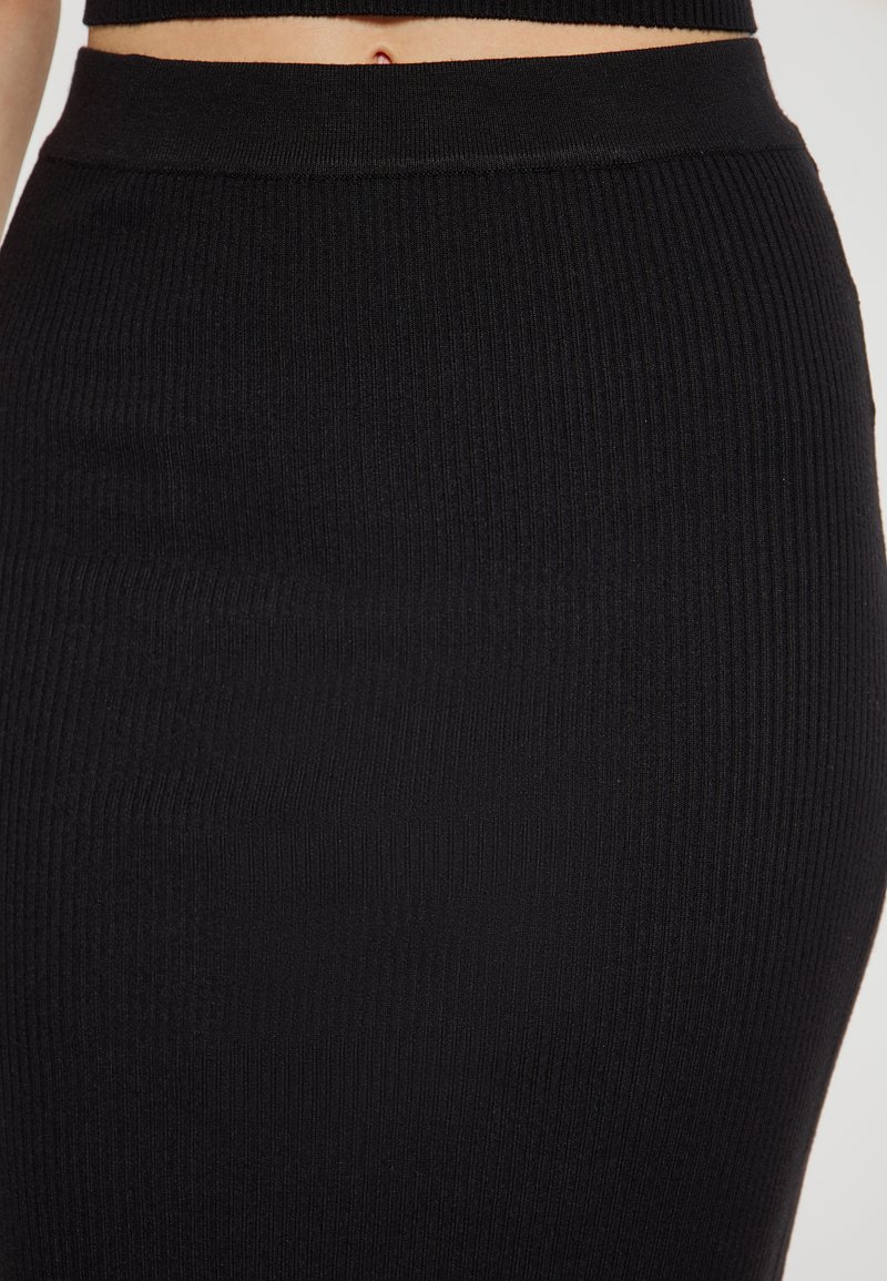 Zwarte geribbelde gebreide rok met een aansluitende silhouet en een soepele elastische tailleband. De stof heeft een fijne textuur met verticale lijnen.