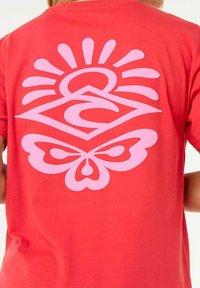 T-shirt rouge avec un grand design graphique rose représentant un soleil et un papillon, avec une texture lisse et des manches courtes.