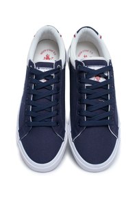 Zapatillas de lona azul marino con detalles en blanco, punta redonda, seis ojales y cordones planos. El interior presenta un logo impreso en una plantilla acolchada.