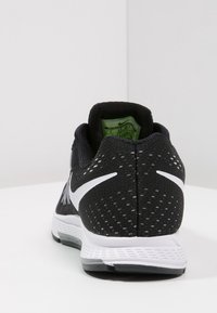 Bottines de sport noires avec une tige en maille texturée, logo Swoosh blanc et col rembourré. La vue arrière montre une étiquette verte et des accents de semelle grise.