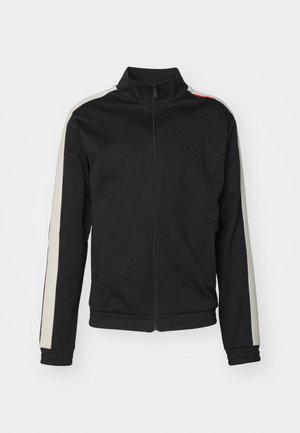 Fekete zipzáras dzseki magas gallérral, fehér oldalsávokkal és textúrált mintával. Két elülső zsebbel és bordás mandzsettákkal rendelkezik.