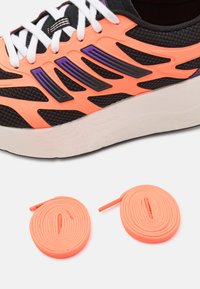 Čierna atletická obuv s oranžovými a fialovými sieťovinami, bielymi šnúrkami a bielou podrážkou. Súčasťou sú dva páry okrúhlych oranžových šnúriek.