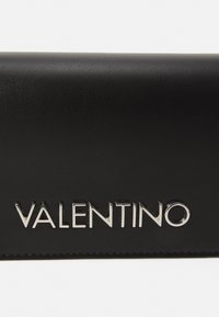 Portafoglio in pelle nera con una texture liscia e un prominente logo argento "VALENTINO". Forma compatta e rettangolare.