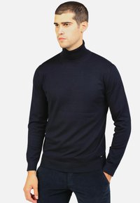 Maglione a collo alto di colore blu navy, realizzato in un tessuto a coste. Presenta maniche lunghe e un design aderente con un discreto dettaglio del logo sull'orlo.